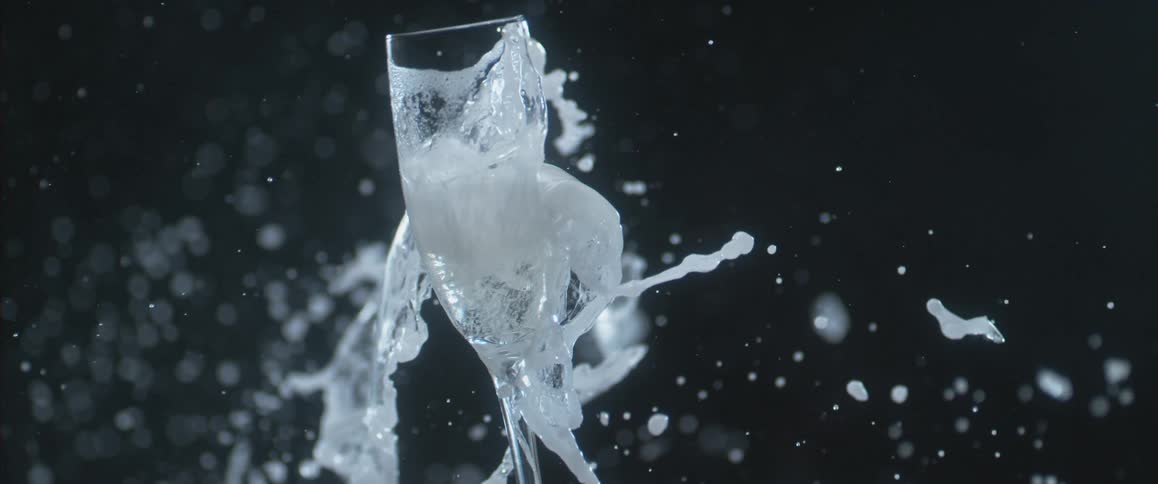 A glass filled with liquid is shattered as the water flies everywhere