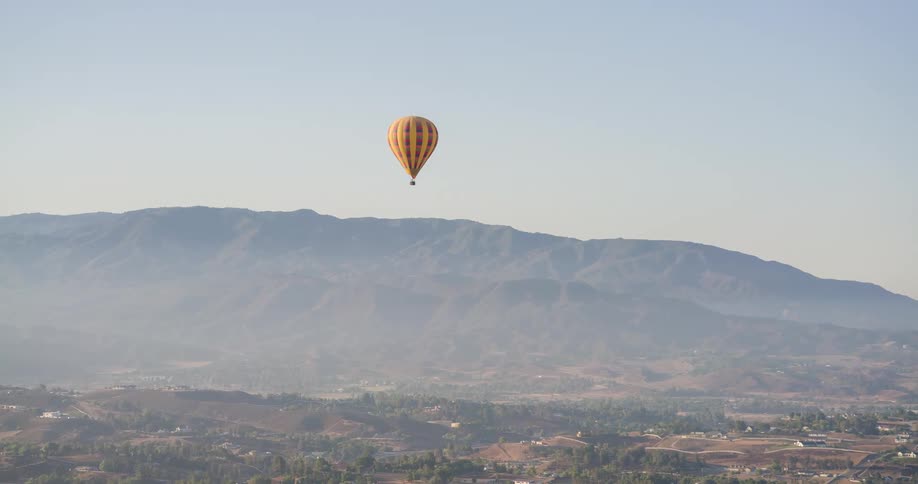 Predominantly yellow balloon flying in an area with mountains