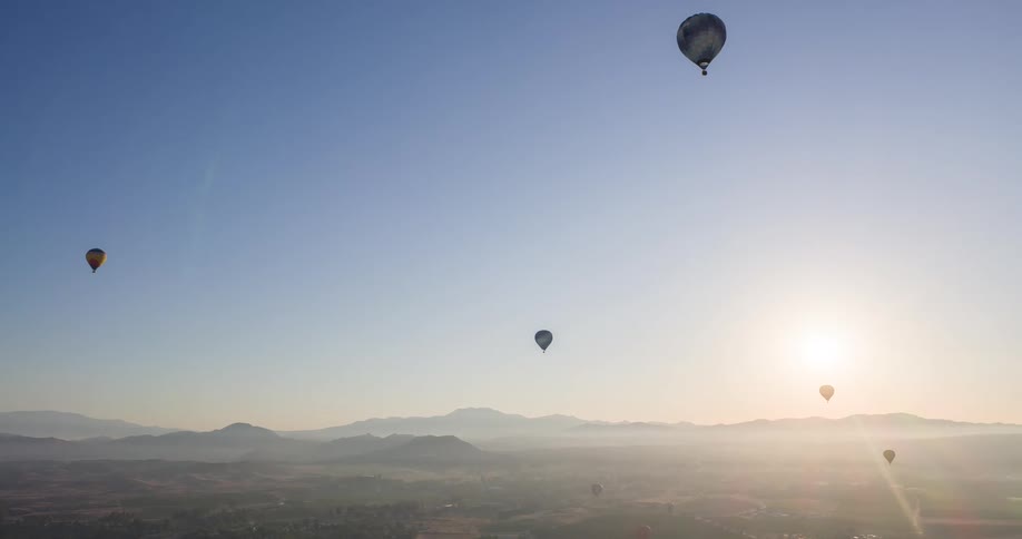 Hot air balloons flying over a mountainous landscape at sunrise