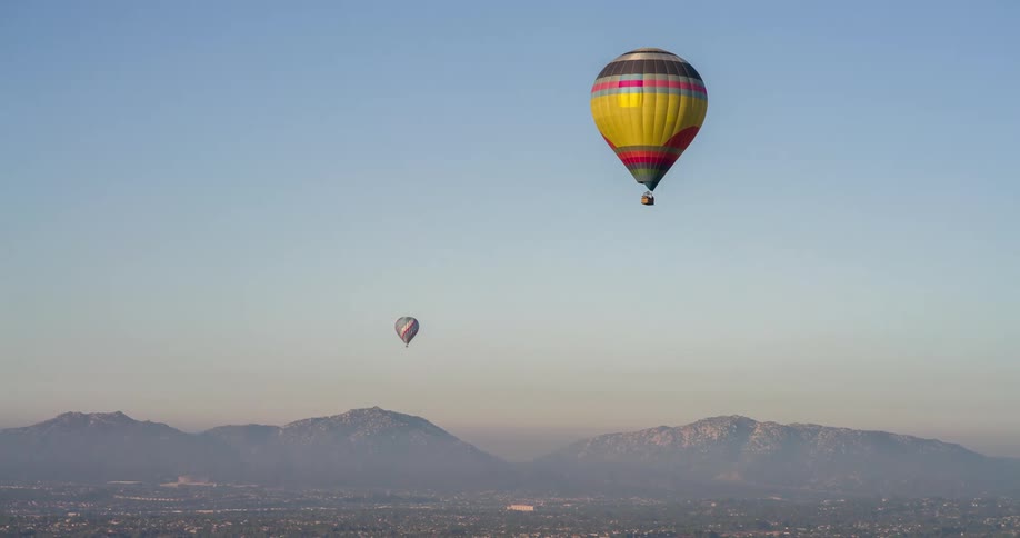 Hot air balloons float above a fog covered town located near low mountains