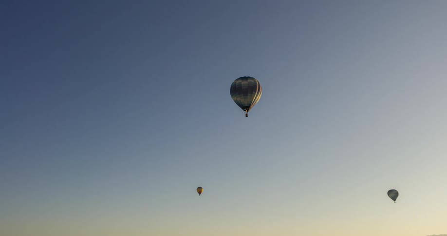 Three hot air balloons drift across a clear blue sky at dusk