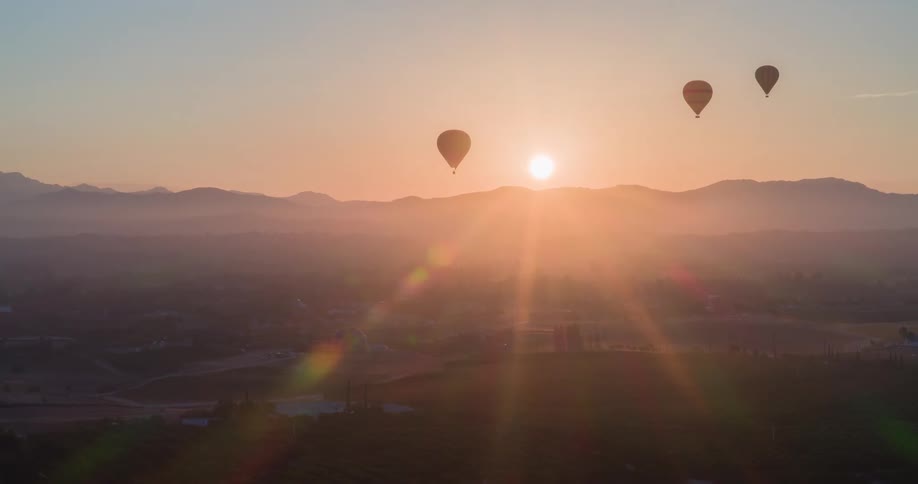 Several hot air balloons ascend into the sky against a tranquil sunrise over a misty mountainous landscape