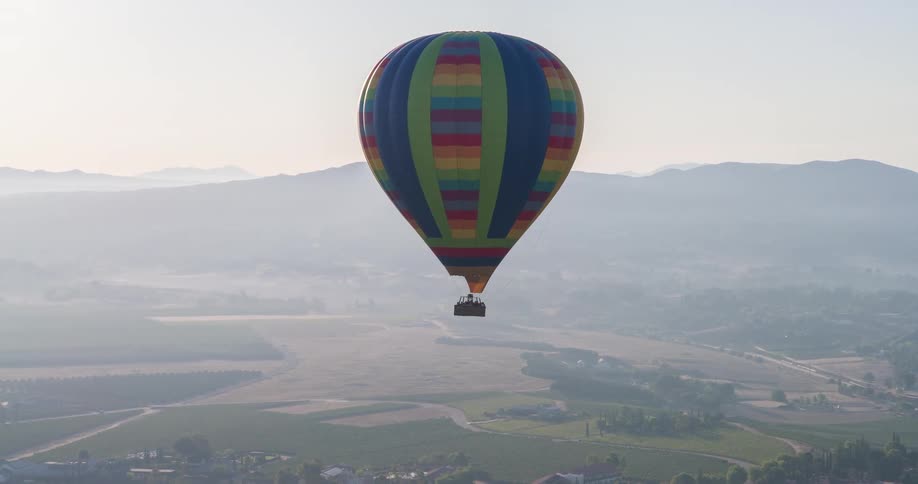 Colorful balloon flying during the day with the silhouette of mountains on the horizon