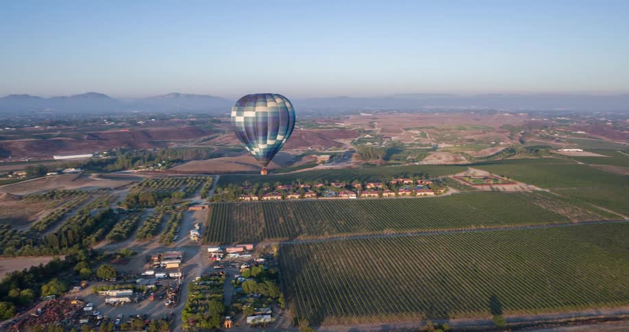 A hot air balloon flying in the sky with another balloon nearby mountains in the background and many cars on the ground below