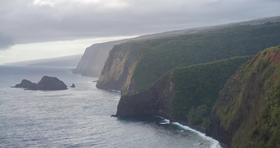 A coastline with steep cliffs covered in lush green vegetation next to the dark blue ocean with several small islands off the coast under a cloudy sky
