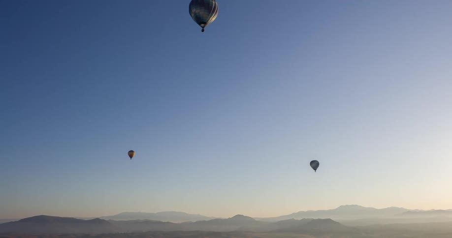 Hot air balloons float above foggy mountainous terrain