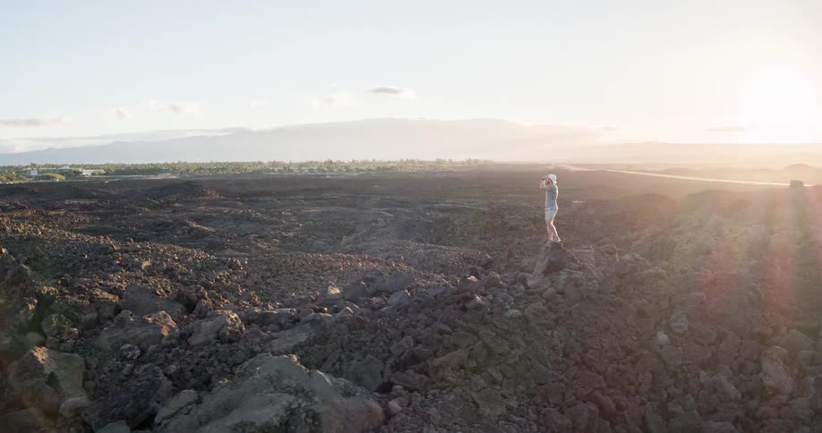 A man stands on the peak of a rock on a rocky island covered with a large spread of stones and rock formations at midday
