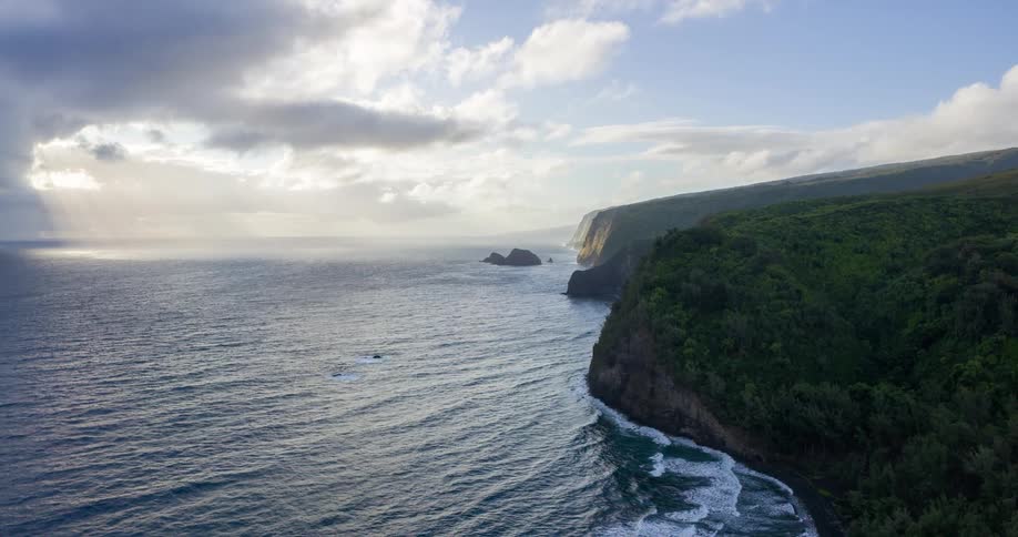 A rocky coast with ocean waves hitting the shore at midday under a cloudy sky