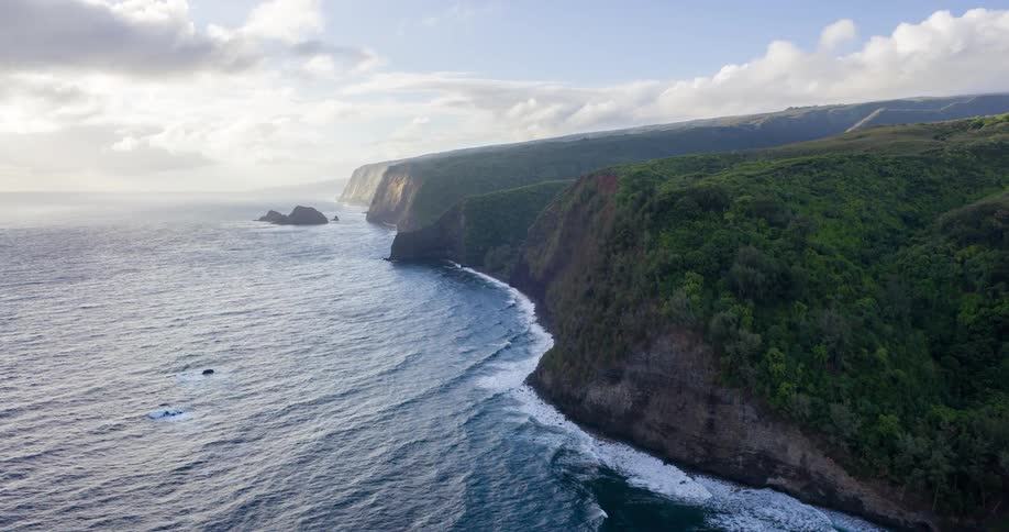 An aerial view shows a stunning rugged coastline with lush green cliffs plunging into the deep blue ocean