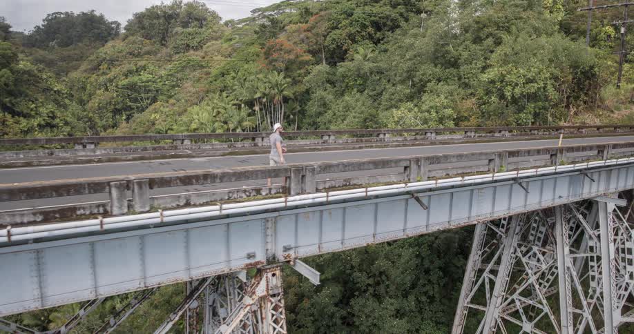 Man walking across a bridge in a wooded area