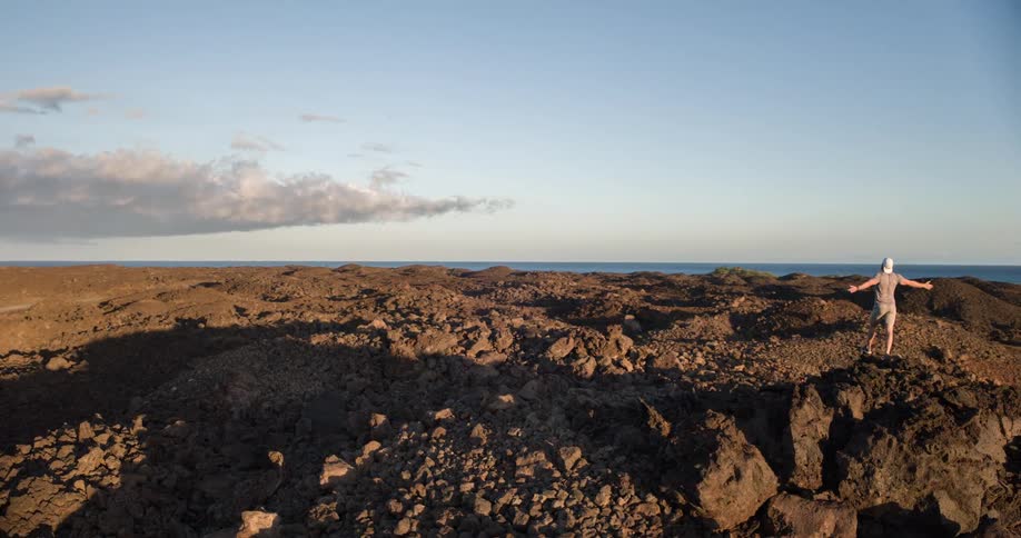 Man with open arms in a rocky environment with the sea in the background