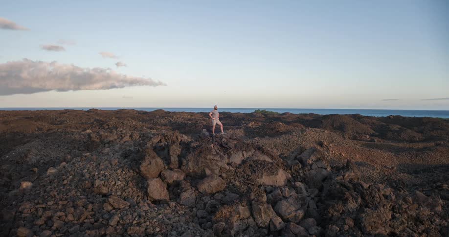 A man wearing shorts stands on a rock peak at midday