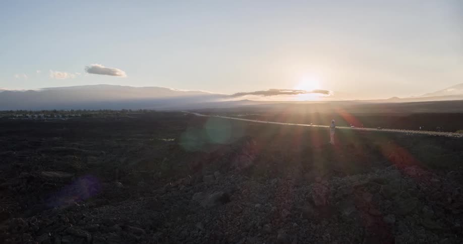 Person in a rocky environment with mountains and the sunset on the horizon