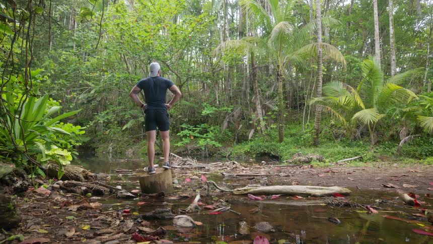 Man standing on a log observing a stream in the forest
