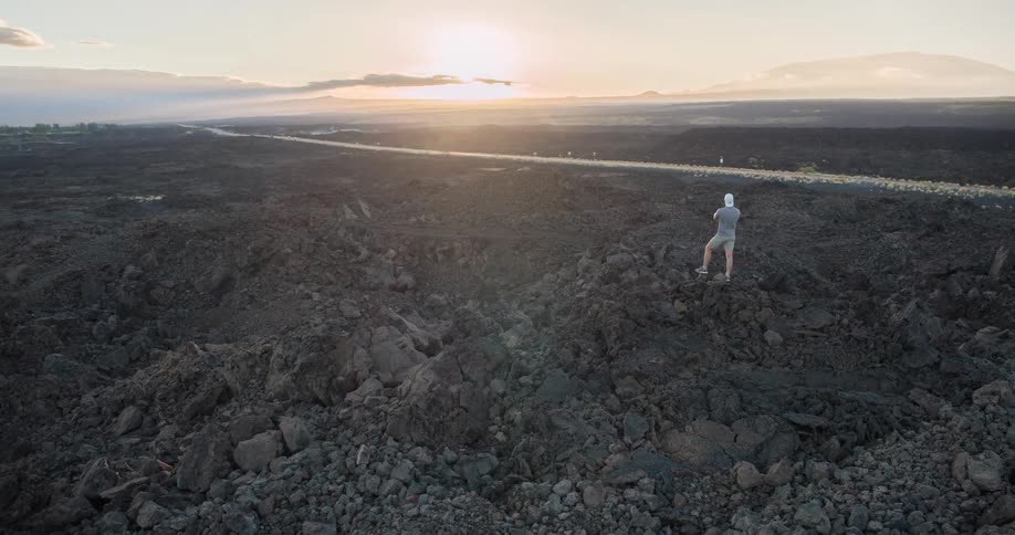 A man stands on the peak of a rock on a rocky island covered with a large spread of stones and rock formations at midday