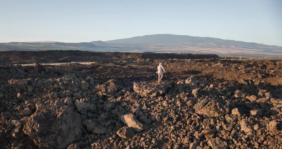 A man carefully climbs a vast volcanic lava field eventually reaching the top to survey the stunning coastal landscape