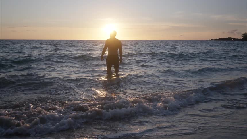Person walking in shallow ocean water during sunset