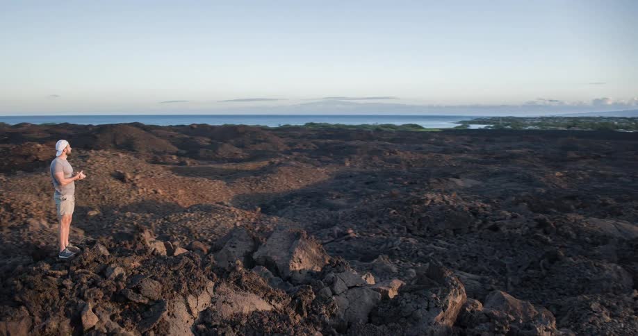A man stands on the peak of a rock on a rocky island covered with a large spread of stones and rock formations at midday