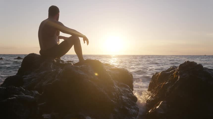 Man sitting on rocks by the sea watching the sunset