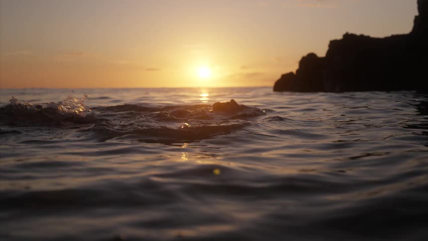 A man swimming backstroke in the ocean with the orange setting sun in the distance