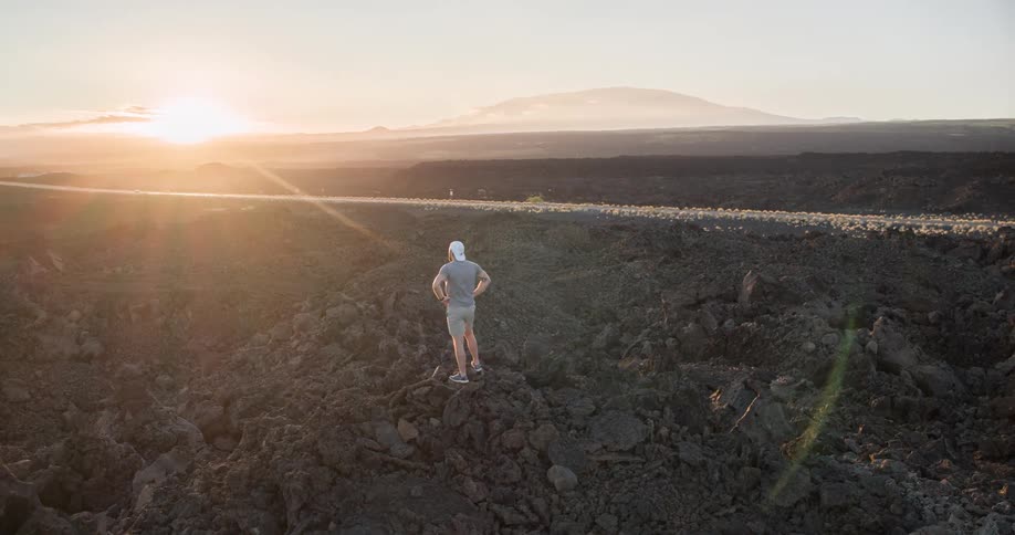 Person standing on solidified lava terrain watching the sunset