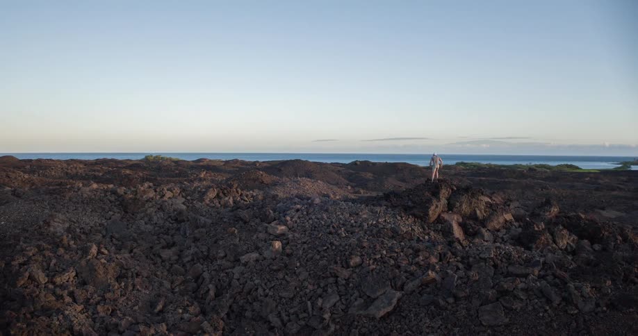 Person walking on dark rocky terrain with the ocean in the background