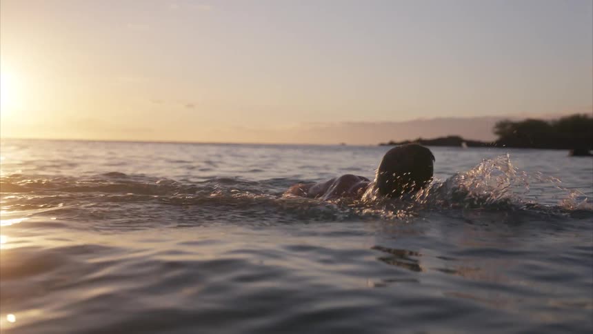 Person swimming in the sea towards the sunset
