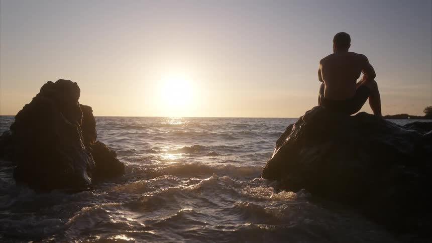 Man sitting on a rock by the sea watching the sunset