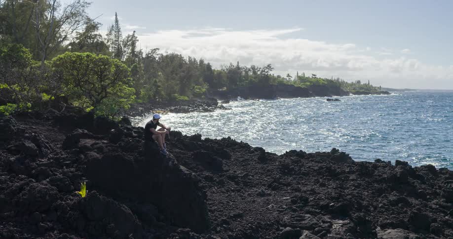 Person sitting on black volcanic rocks by the sea