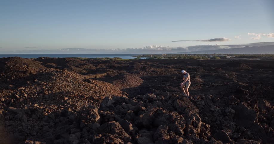 The man is climbing on the rocks by the shore