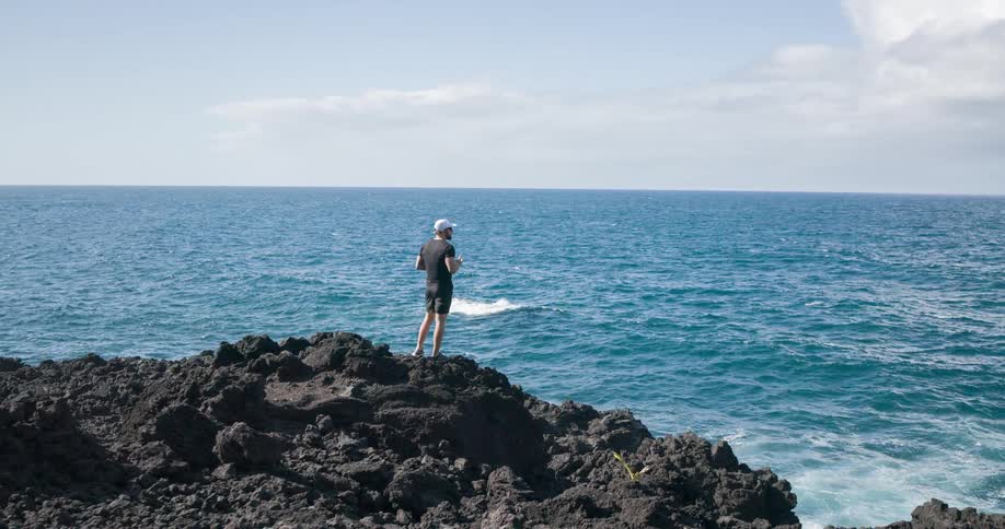 A man is standing on the rocks holding a water bottle