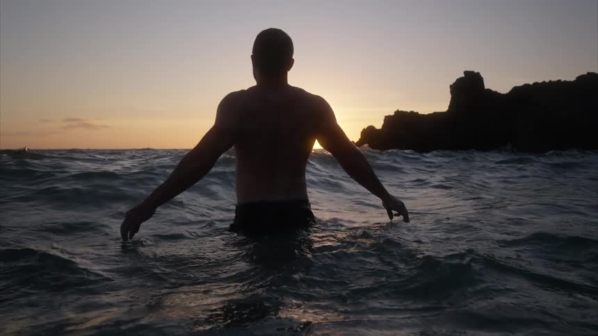 The man wades through the water at sunrise