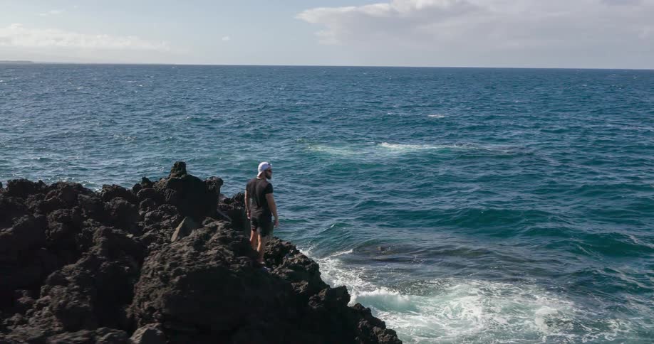 Drone view of a man standing on a rocky cliff on the ocean coast