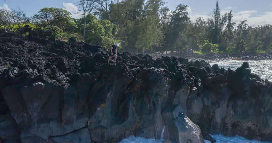 A man standing on a rocky cliff over the ocean with a forest behind it