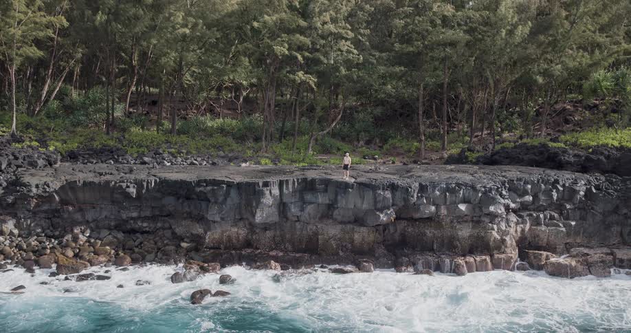 Young man walking at the edge of a cliff watching waves roll in and crash against the rocks