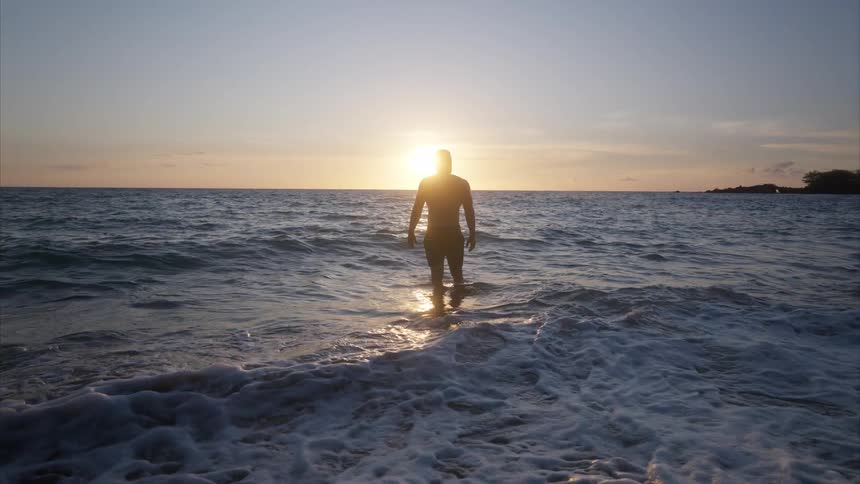 Silhouette of a man at sunset in the sea on the beach