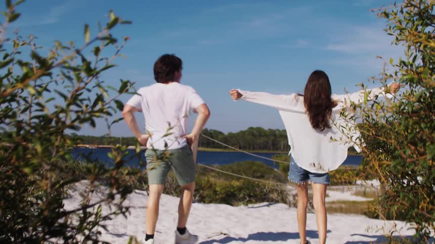 A couple holding hands runs toward a lakeshore as the man playfully lifts the woman