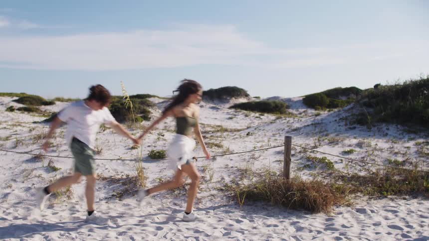 Couple runs hand in hand across the sand on a sunny beach