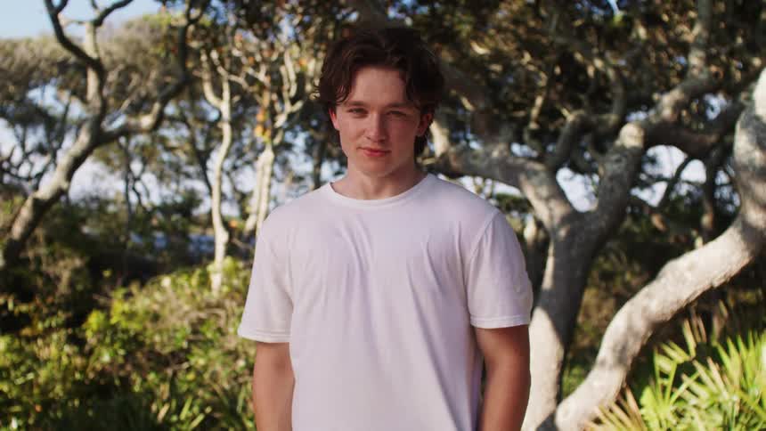 The boy is standing in front of the trees