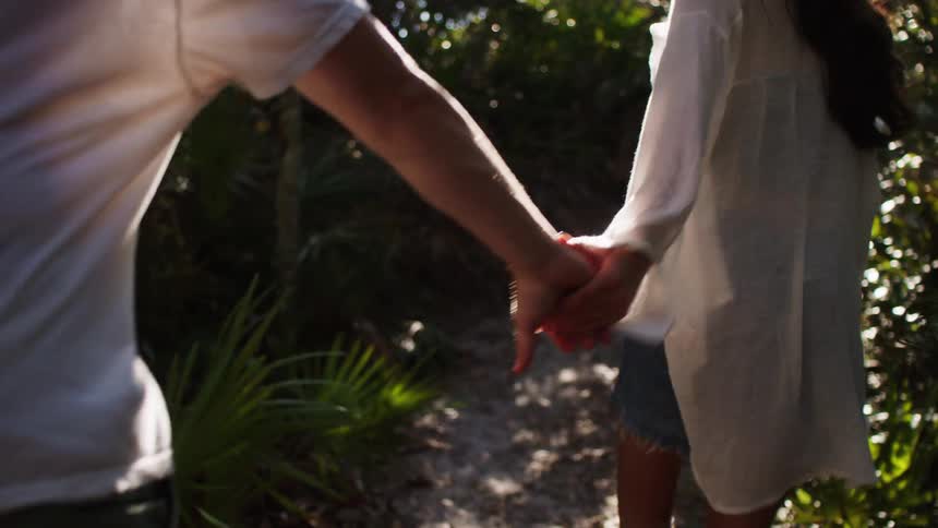 A young couple walks in the jungle holding hands at midday