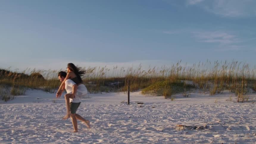 Man carrying a woman on his back while walking along the beach