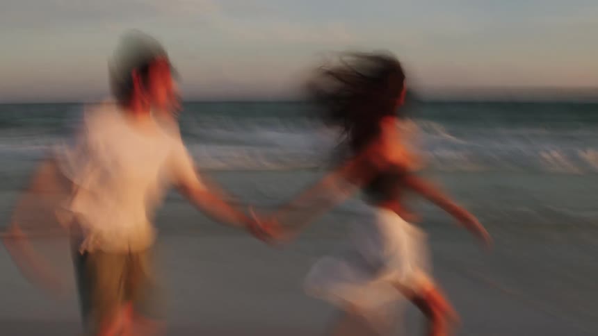 Couple holding hands running on the beach in the late afternoon