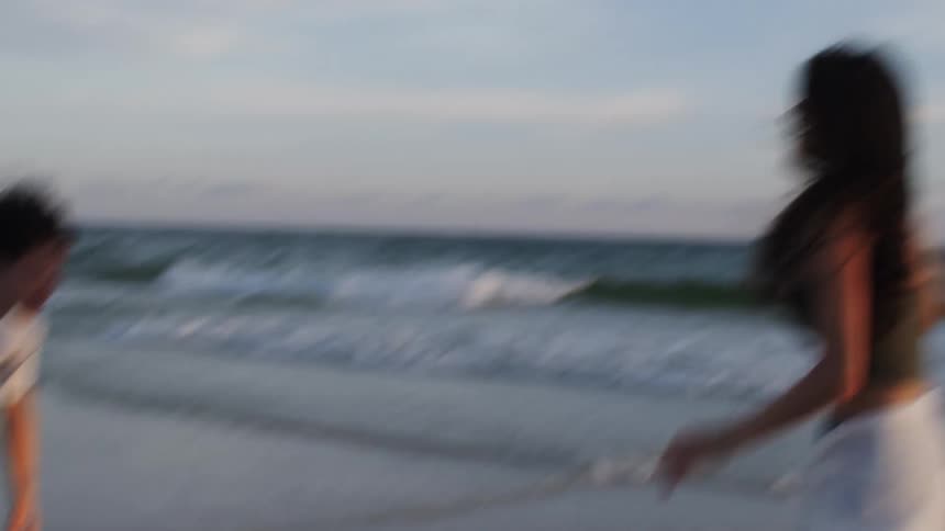 A man and woman on vacation at the beach are playing and having fun on the sand with the woman wearing sunglasses at midday