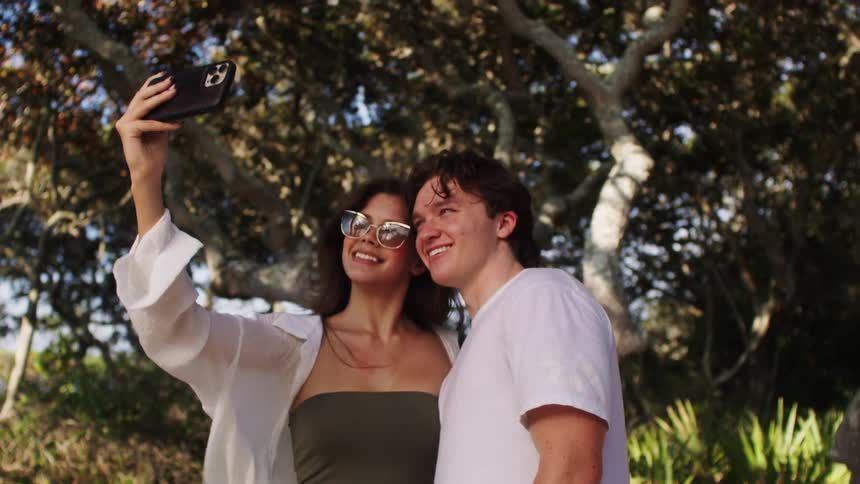 Young couple taking a selfie front of a tree near the coast