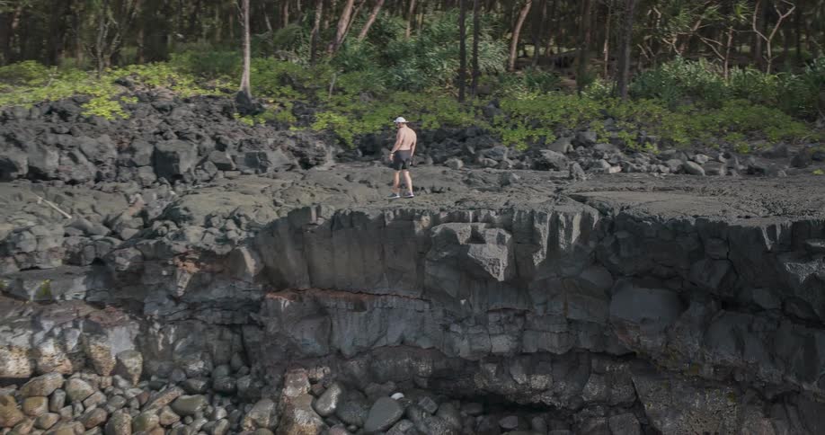 Man walking along the edge of a cliff as waves crash into the rocks below