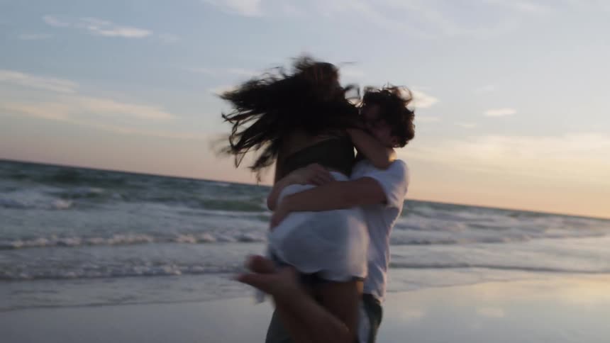 Young male spinning his girlfriend on the shoreline at the beach at sunset