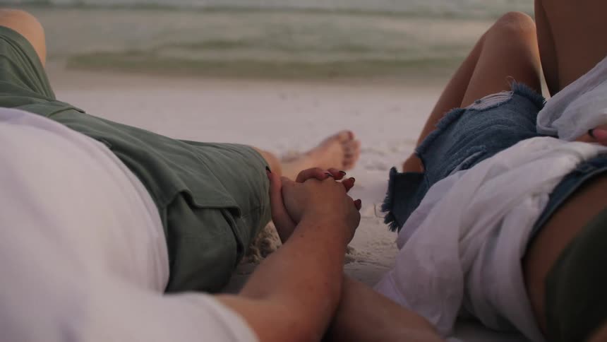 Couple lying on the beach holding hands