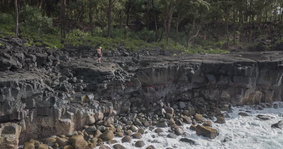 Young man leaps across rocks near the edge of a cliff as waves crash into rocks below