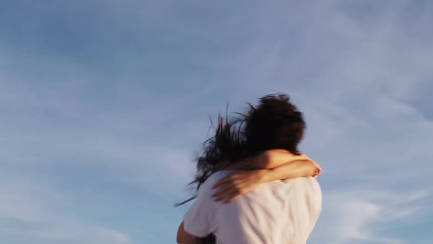 Couple embraces tightly outdoors under a blue sky