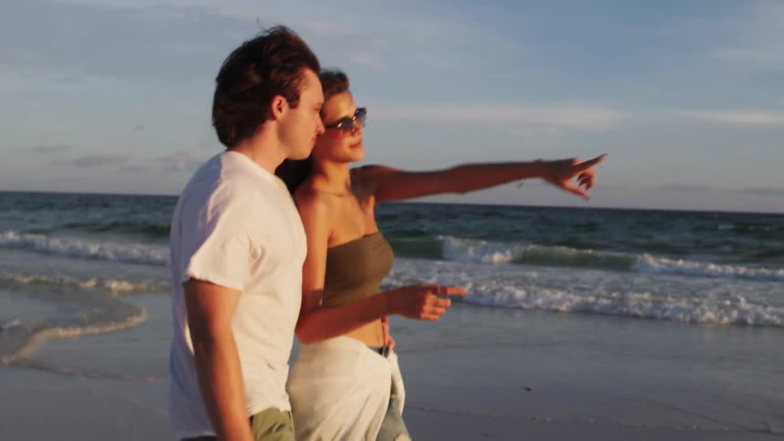 Young couple walk together on the beach talking as waves roll into shore